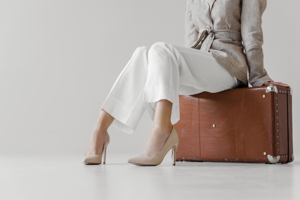 image recadrée d'une femme élégante en veste de lin assise sur une valise vintage isolée sur fond gris
  - Photo, image