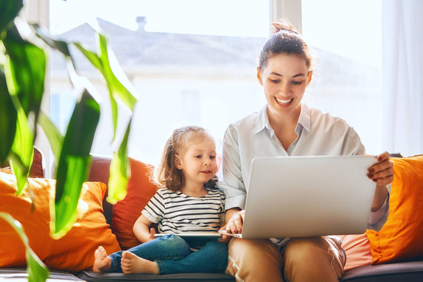 Happy loving family. Young mother and her daughter girl play in room. Funny mom and lovely child are having fun with laptop. - Фото, зображення