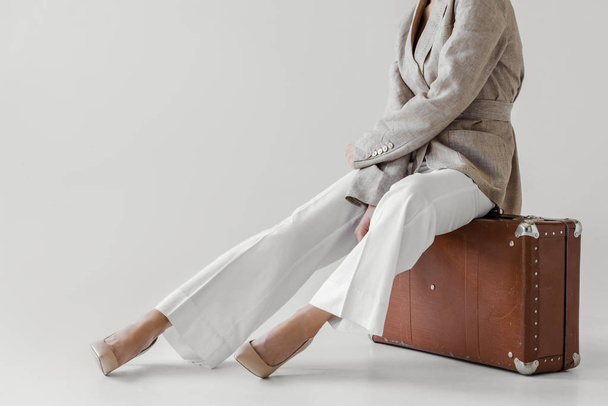 cropped image of stylish woman in linen jacket sitting on vintage suitcase isolated on grey background  - Foto, imagen