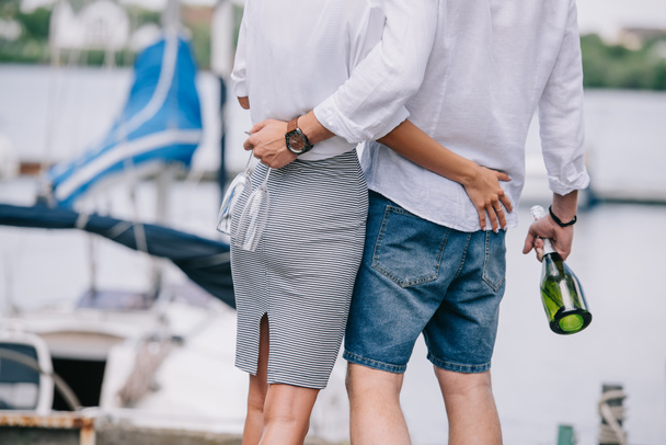 cropped shot of young couple holding wine glasses and bottle, hugging at seaside - Foto, Imagem