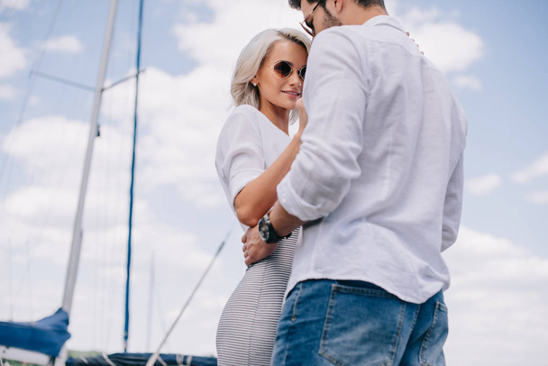 low angle view of beautiful stylish young couple in sunglasses hugging on yacht - Photo, Image