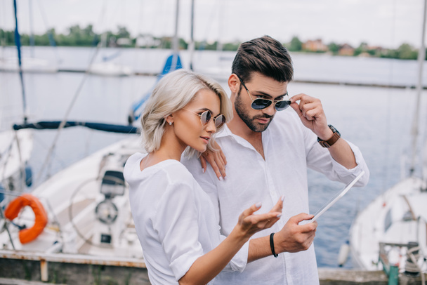 beautiful stylish young couple in sunglasses using digital tablet on yacht - Фото, зображення