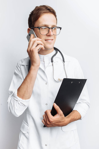 Young and handsome doctor talking on the phone with patients, Intern student with folder in hand, white background, - Фото, зображення
