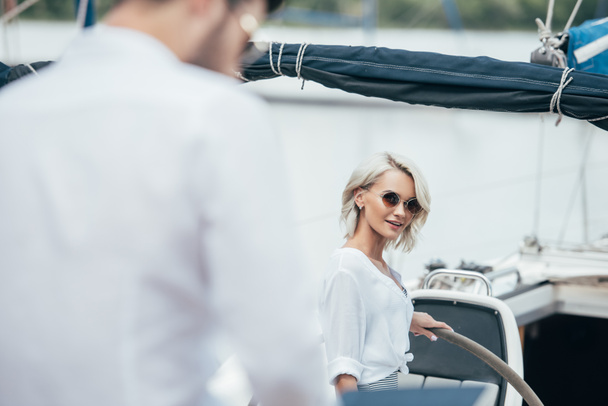 вибірковий фокус красивої усміхненої дівчини в сонцезахисних окулярах дивиться на людину на яхті
 - Фото, зображення