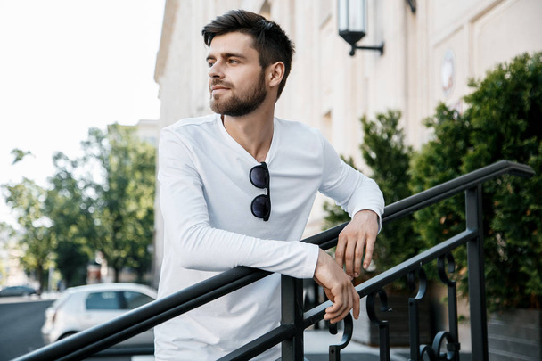 A young man travels through the streets of the city. Boy in sunglasses Stylish man near the building. The man sits on a whip. Beard and hair in a stylish guy. Senior student after studying. - Foto, afbeelding