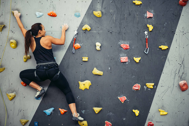 Woman practicing rock climbing on artificial wall indoors. Active lifestyle and bouldering concept. - Photo, image