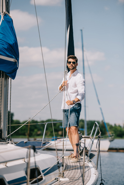 vista completa di bel giovane uomo in occhiali da sole in piedi su yacht
 - Foto, immagini