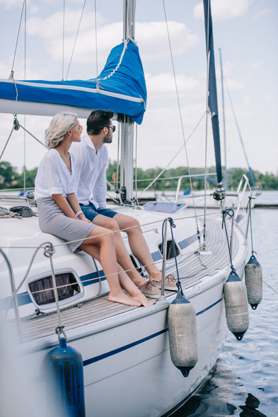 beautiful young couple sitting together on yacht and looking away - Foto, Imagen