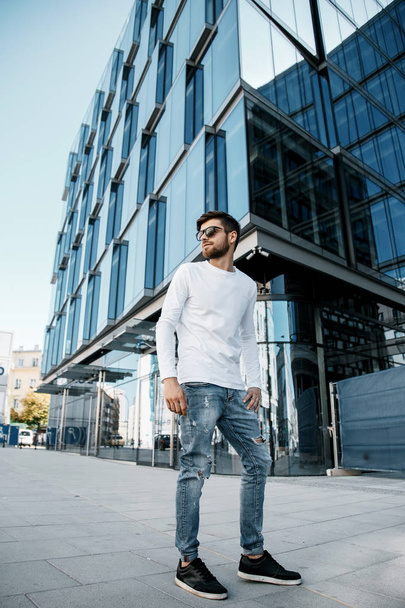 A young man travels through the streets of the city. Boy in sunglasses Stylish man near the building. The man sits on a whip. Beard and hair in a stylish guy. Senior student after studying. - Foto, Imagen