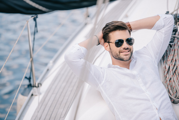 beau jeune homme souriant dans des lunettes de soleil reposant avec les mains derrière la tête sur le yacht
 - Photo, image