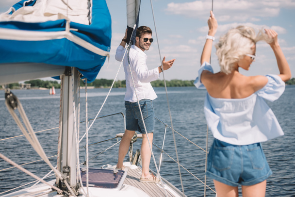 smiling young man in sunglasses looking at beautiful girl on yacht - Photo, Image
