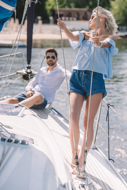 mladý muž v sluneční brýle sedí a při pohledu na krásnou dívku na jachtě - Fotografie, Obrázek