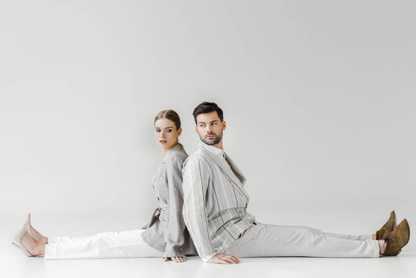 couple of fashionable models in vintage clothes sitting on floor and leaning back to back on white - Foto, Bild