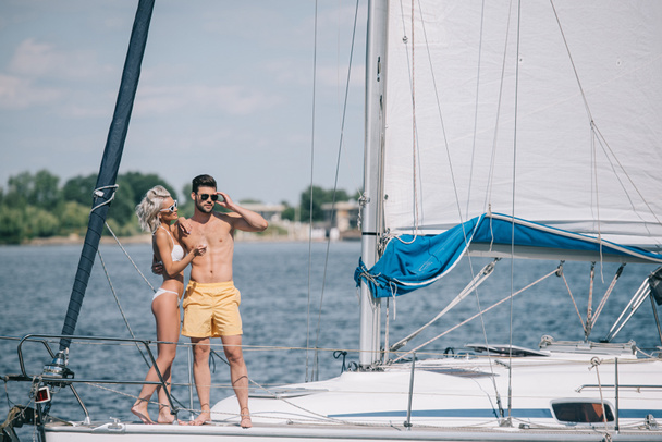 beau jeune couple en maillots de bain et lunettes de soleil debout ensemble sur yacht
 - Photo, image