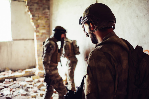 A ppicture of soldiers standing in a rooom near ruined wall. Two of them are standing towards each other while thrid one is looking at them. They are having some rest. - Foto, Bild