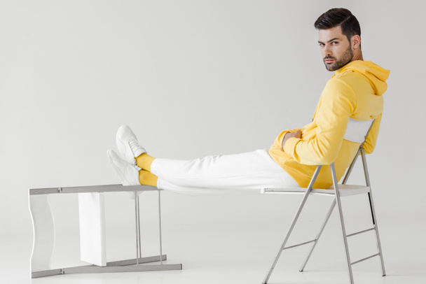 handsome young man in yellow hoodie sitting relaxed on white and looking at camera - Foto, imagen