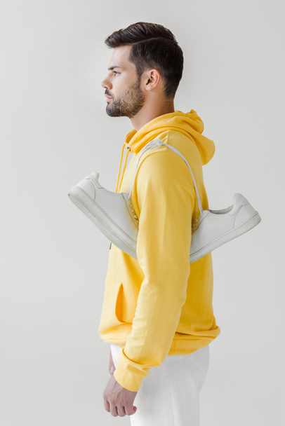 Zijaanzicht van de knappe jongeman in gele hoodie met witte sneakers opknoping op schouder geïsoleerd op wit - Foto, afbeelding