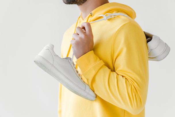 cropped shot of young man in yellow hoodie with white sneakers hanging on shoulder isolated on white - Fotó, kép