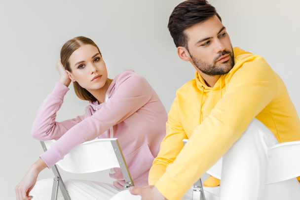young male and female models in pink and yellow hoodies sitting on chairs isolated on white - Foto, imagen