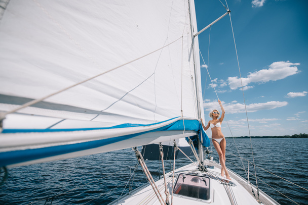 distant view of attractive young woman in swimwear standing on yacht  - Foto, Bild