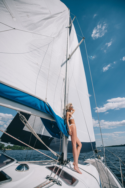 vista laterale di attraente giovane donna in costume da bagno in piedi su yacht
  - Foto, immagini
