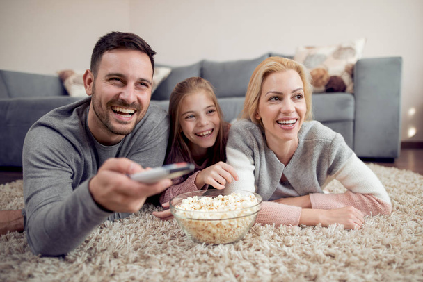 Father, mother and daughter lying on floor and watching TV. - Photo, image