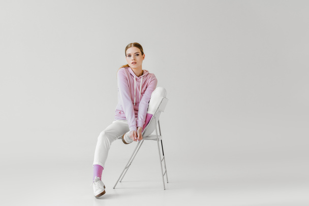 beautiful young woman in pink hoodie sitting on chair on white and looking at camera - Photo, Image