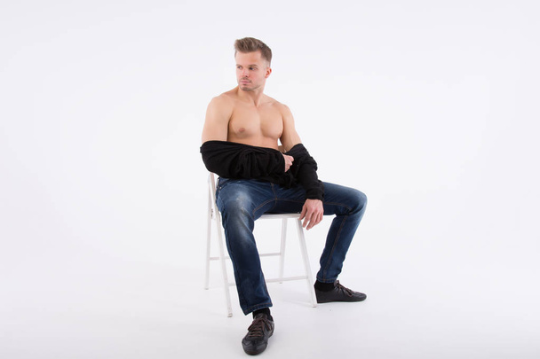 Όμορφος νεαρός είναι ανάπαυση. Η shirtless άντρας κάθεται στον καναπέ. Μυώδης και σέξι. Γκρι φόντο - Φωτογραφία, εικόνα