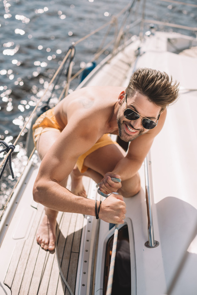 uomo senza maglietta sorridente in occhiali da sole tirando corda su yacht
  - Foto, immagini