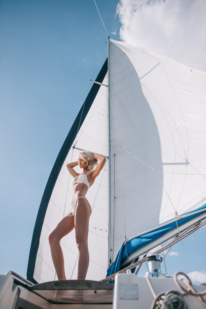 low angle view of beautiful young woman in bikini posing on yacht  - Photo, image