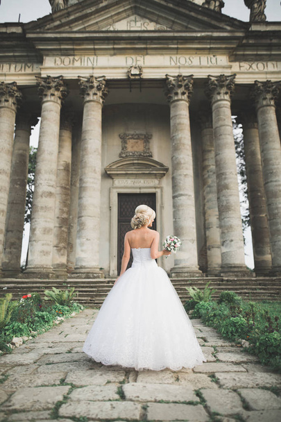 Beautiful elegant bride with perfect wedding dress and bouquet posing near old castle - Foto, immagini