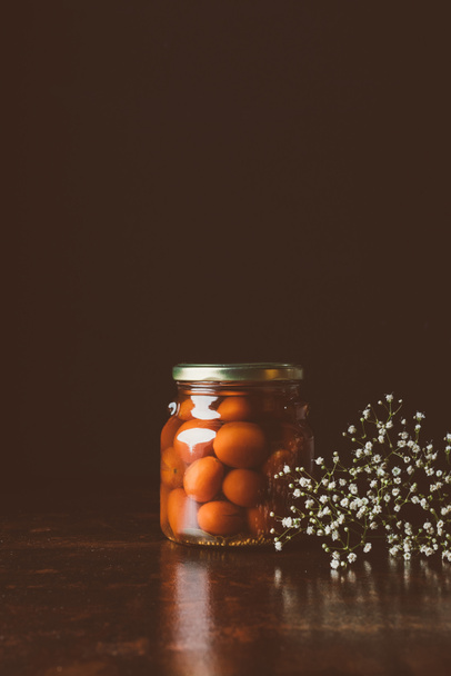 glass jar with preserved red tomatoes on wooden table in dark kitchen  - Foto, Imagen