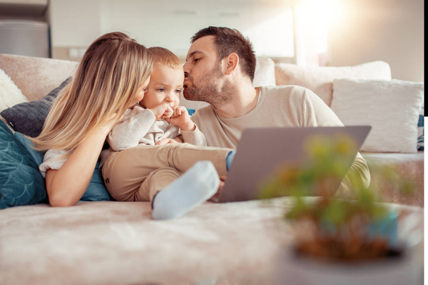 Hymyilevät nuoret vanhemmat ja keskittynyt poika käyttävät kannettavaa tietokonetta kotona
. - Valokuva, kuva