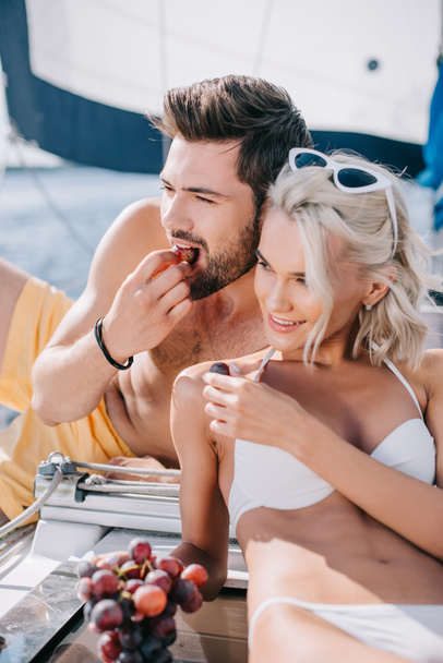 sourire jeune couple en maillot de bain manger des raisins sur le yacht
  - Photo, image