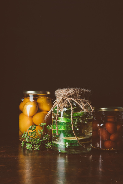 glass jars with preserved vegetables on wooden table in dark kitchen  - Foto, afbeelding