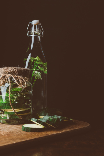 preserved zucchini in glass jar and fresh cut zucchini on wooden board in kitchen - Foto, Imagen