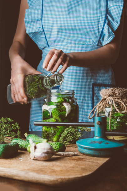 cropped image of woman preparing preserved cucumbers and pouring water into jar at kitchen - Photo, Image