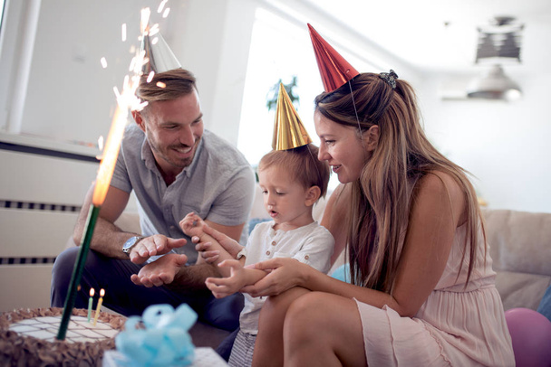 Happy family celebrating a birthday together at table at home in the living room. - Фото, зображення