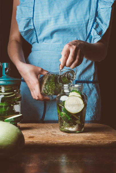 cropped image of woman preparing preserved zucchini and pouring water into jar at kitchen - Photo, Image