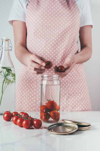 abgeschnittenes Bild einer Frau, die in der Küche Tomaten in Glasgefäße legt - Foto, Bild