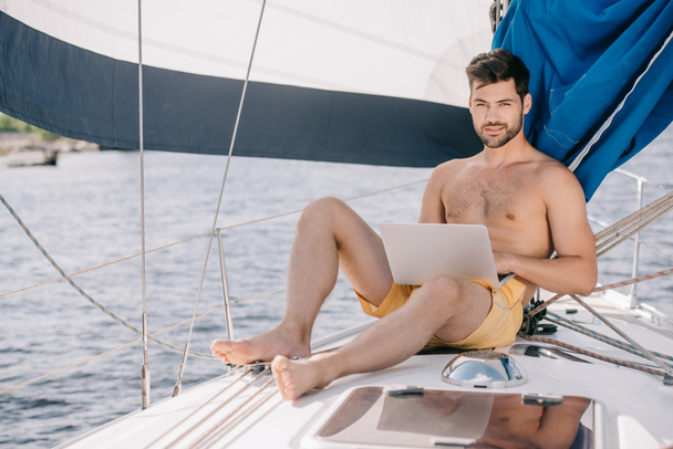 красивый мужчина без рубашки в плавках с ноутбуком на яхте
 - Фото, изображение