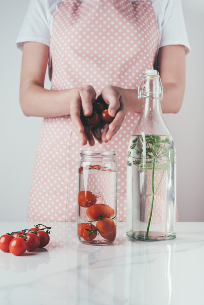 rajattu kuva nainen laittaa tomaatteja lasipurkkiin vedellä keittiössä
 - Valokuva, kuva