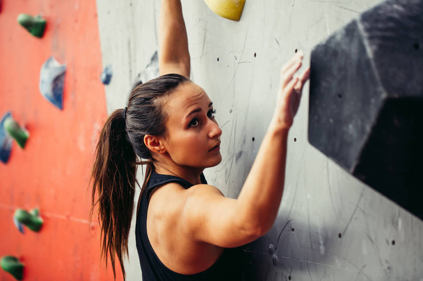 Beautiful young strong woman climbing on red artificial wall top view. - 写真・画像