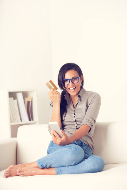 Retrato de mujer feliz comprando en línea con tableta de digialt y tarjeta de crédito en un sofá en casa
 - Foto, Imagen