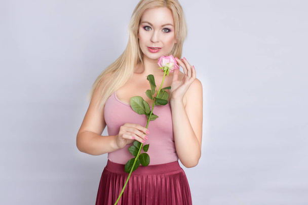 A cute young blonde woman holding a pink rose - Foto, Bild