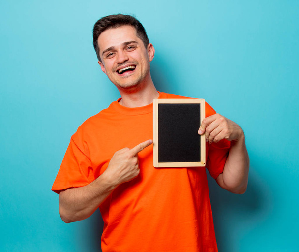 мужчина в оранжевой футболке с маленькой доской
 - Фото, изображение