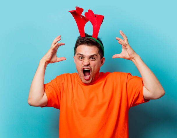 мужчина в оранжевой футболке с рождественскими оленьими рогами
 - Фото, изображение
