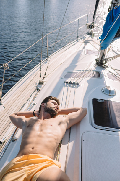 ヨットの上で日光浴を持つトランクの水着で上半身裸の筋肉男のハイアングル  - 写真・画像