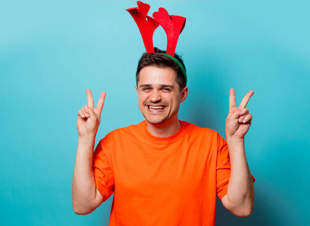 мужчина в оранжевой футболке с рождественскими оленьими рогами
 - Фото, изображение