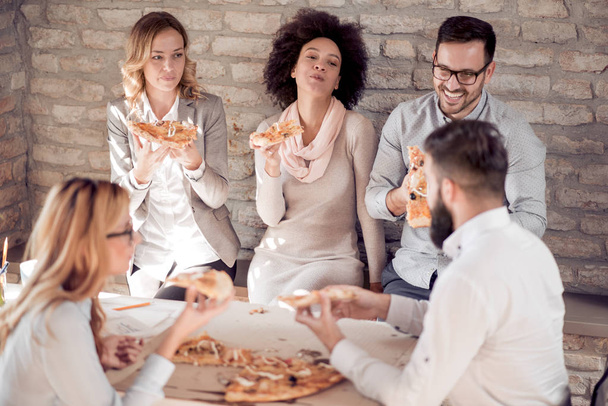 Χαρούμενος νεαρός επαγγελματίες ομάδα τρώγοντας πίτσα στο γραφείο. Έννοιας επιχείρηση, φαγητό και άνθρωποι. - Φωτογραφία, εικόνα